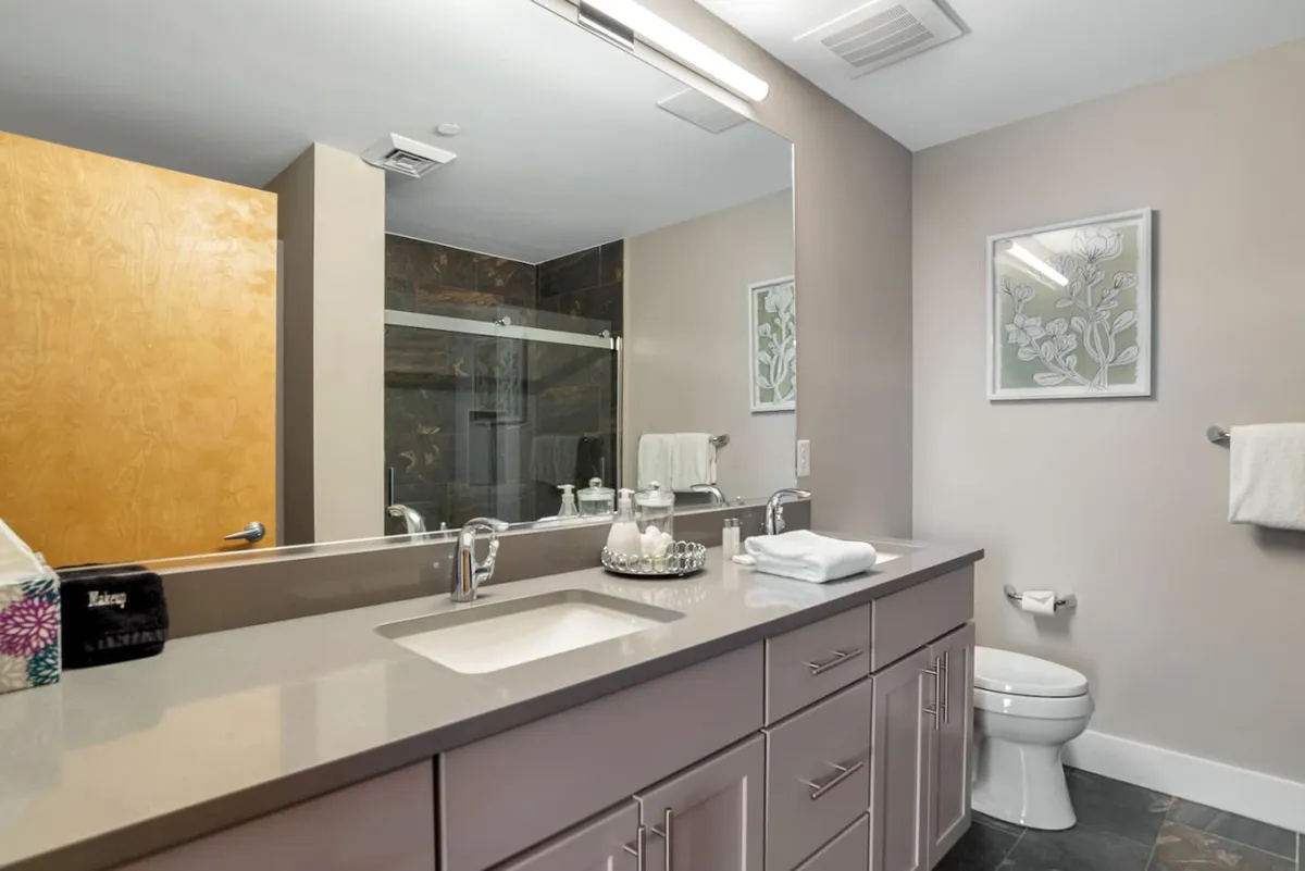 A modern bathroom featuring a vanity sink with a large mirror, framed artwork, and a glass shower enclosure. The space feels fresh and serene, ideal for relaxation and self-care routines.