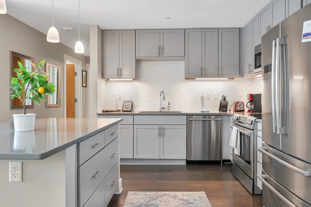 This image showcases a welcoming, contemporary kitchen featuring a central island, stainless steel appliances, grey cabinets, and a decorative plant with lemons. The setting exudes a sense of togetherness, making it perfect for cooking, entertaining, or gathering with family and friends.