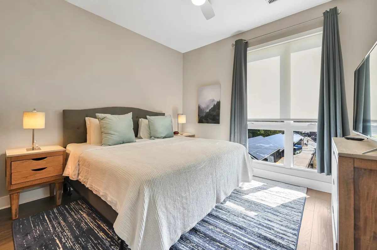 A cozy, serene bedroom featuring a comfortable bed, nightstands, flowing curtains, a window that lets in soft light, and tasteful artwork. The ambiance is restful, supporting relaxation and private moments.